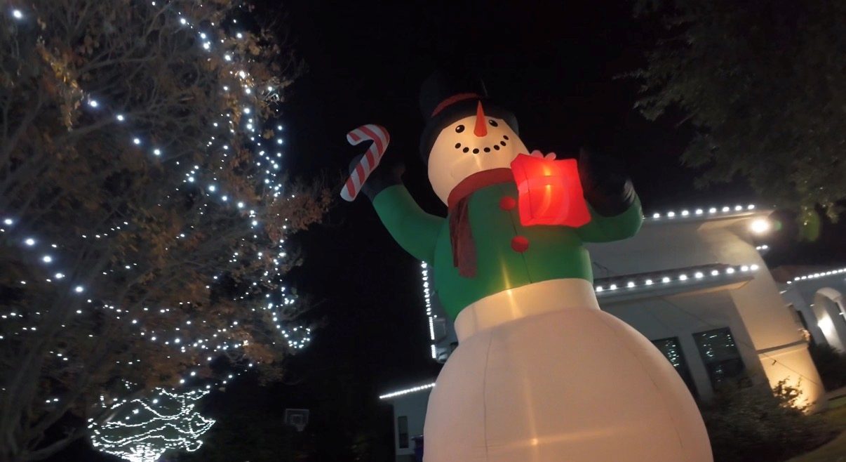 Giant inflatable snowman beside a lit tree and roofline