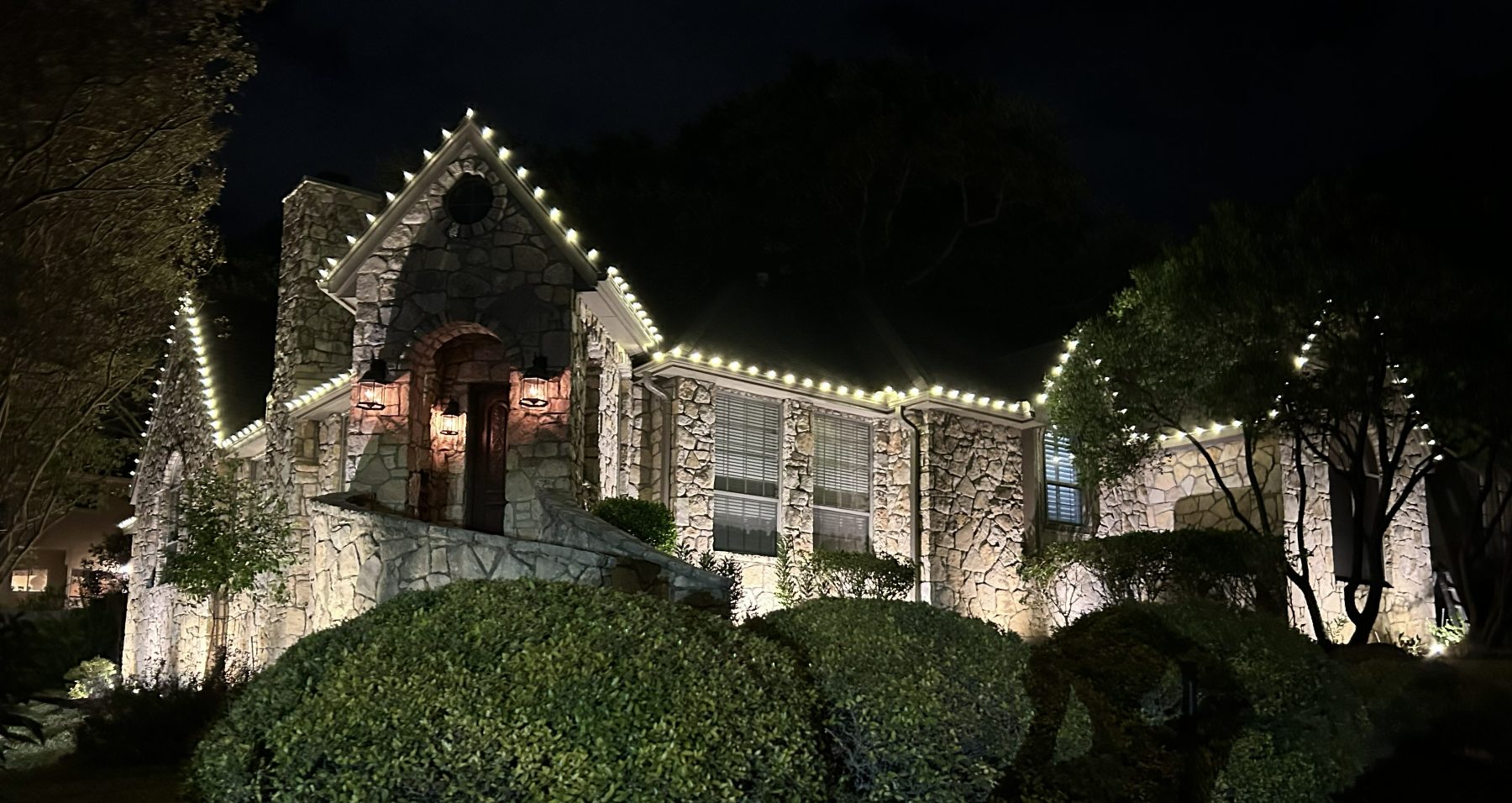 Close view of bright C9 bulbs tracing a stone home's roofline at night