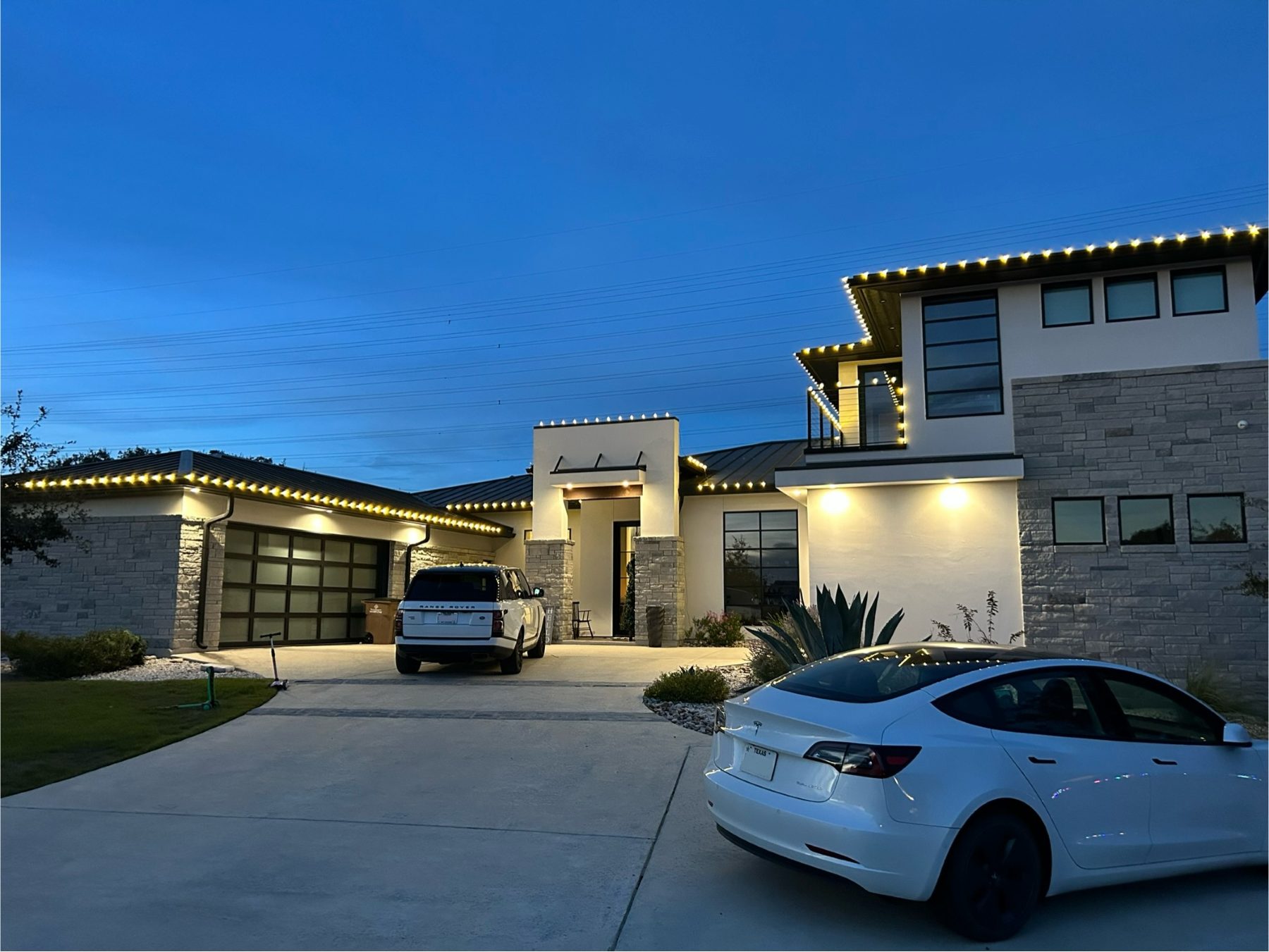 Modern stone and stucco home with warm C9 bulbs along the rooflines at dusk